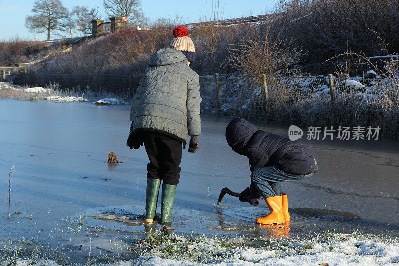 两个男孩在结冰的水坑上玩