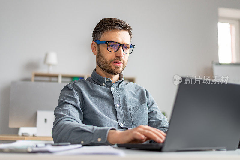 专注的成熟商人在他的办公桌上用笔记本电脑工作，在电脑键盘上打字，检查电子邮件