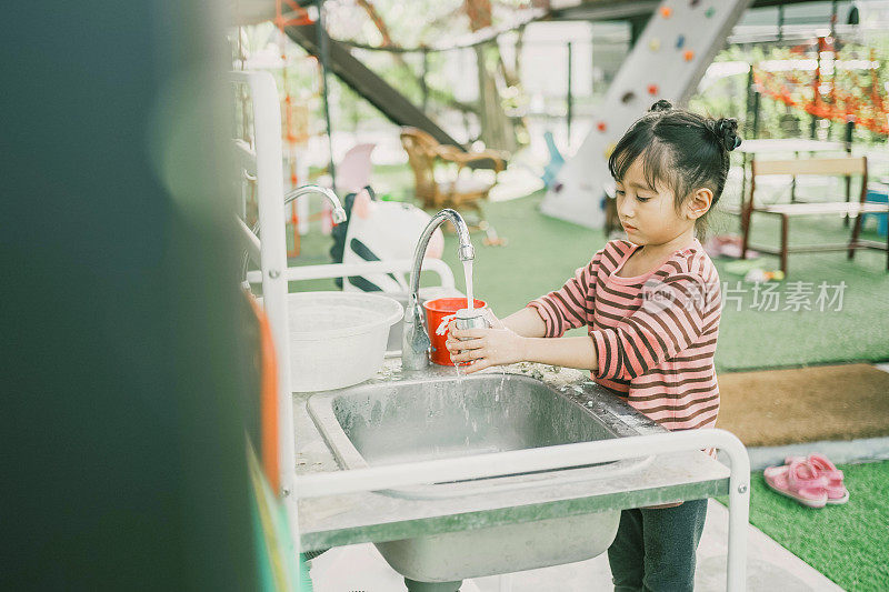 学龄前混合女孩在户外洗涤站洗玩具，蒙特梭利教育学校的实用生活技能活动