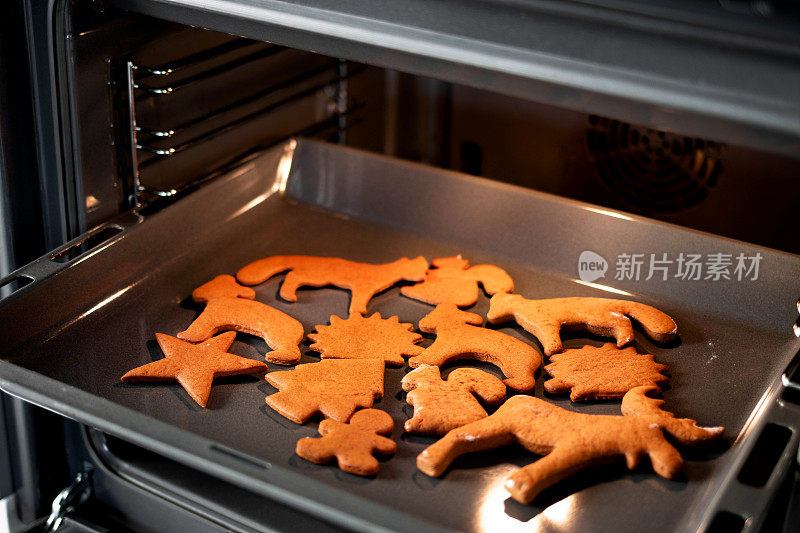 在明亮的厨房里，把圣诞姜饼放在开放式现代烤箱的烤盘上。烤炉里的圣诞饼干——暖暖的灯光，喜庆的气氛。冬季、圣诞节和新年的概念