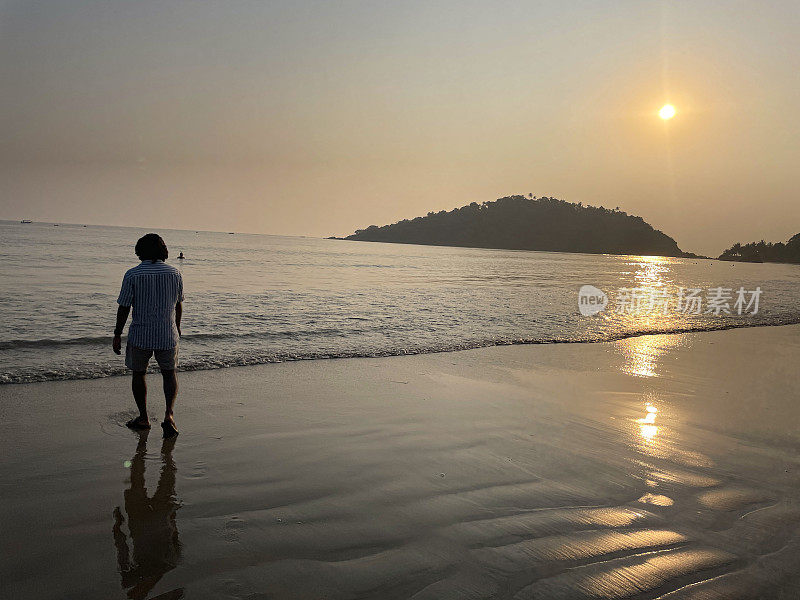 印度人在果阿海滩度假，日落时在海里划桨，印度果阿帕洛莱姆，度假游客赤脚走在海滩上，在水里戏水，后视图，关注前景，复制空间