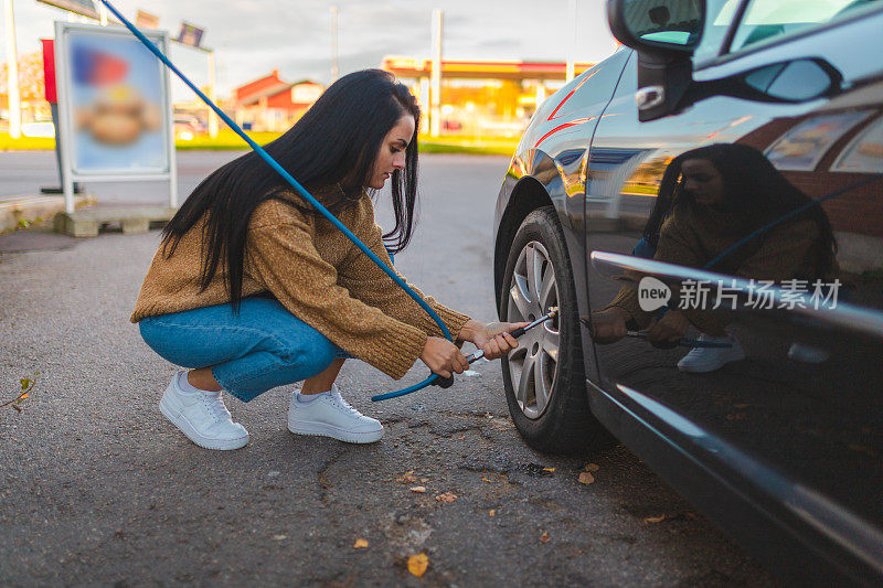 美丽的年轻女子在检查她车子的轮胎气压