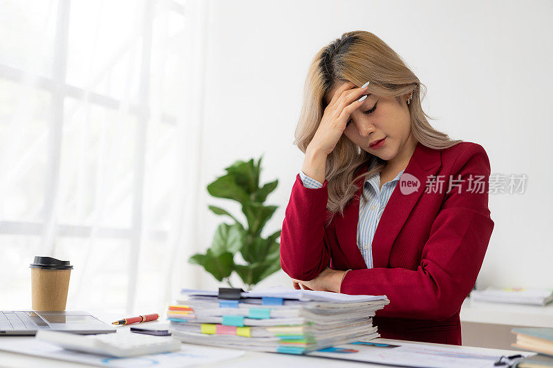 忙于商业财务报告的亚洲女商人感到压力和恼怒。在笔记本电脑和太多文件面前工作感到疲惫