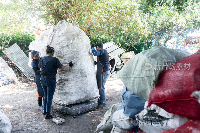 年轻的西班牙裔工人正在称重一大袋可回收塑料