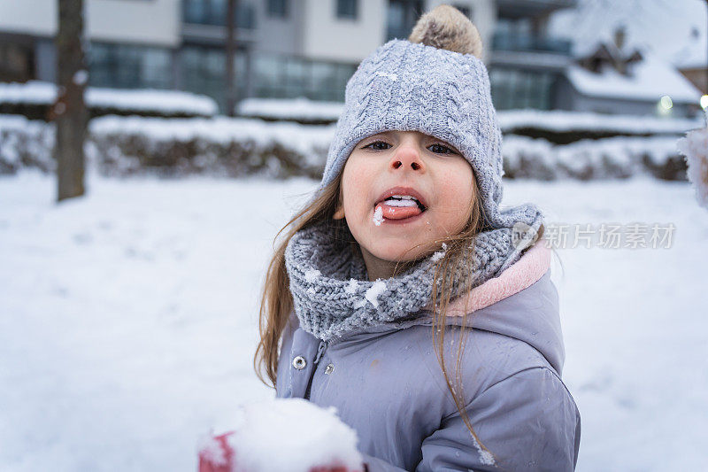 一个蹒跚学步的白人女孩，在冬天玩耍时舔着雪球