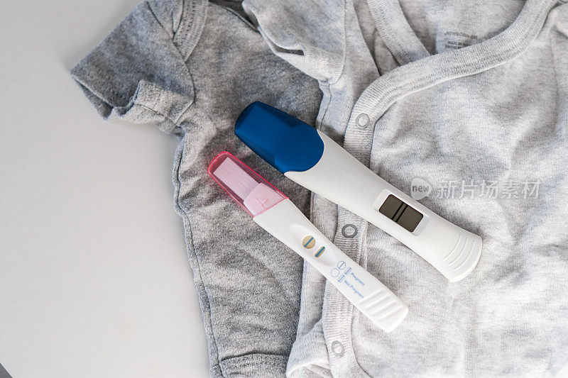 婴儿衣服上的两个阳性妊娠试验的俯视图