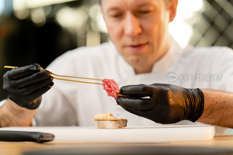 戴着黑色手套的厨师用镊子夹一块生腌肉块法棍面包的脸部特写