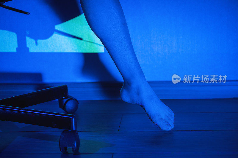 一个女人坐在电脑椅上，在蓝光下伸伸腿