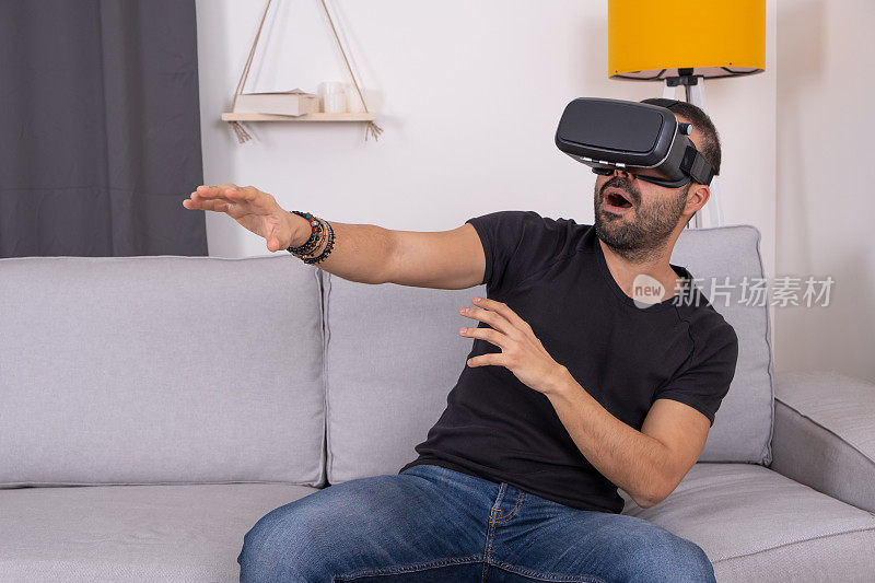 年轻人戴着VR头盔在家里的沙发上兴奋地打着手势，未来科技，教育视频游戏