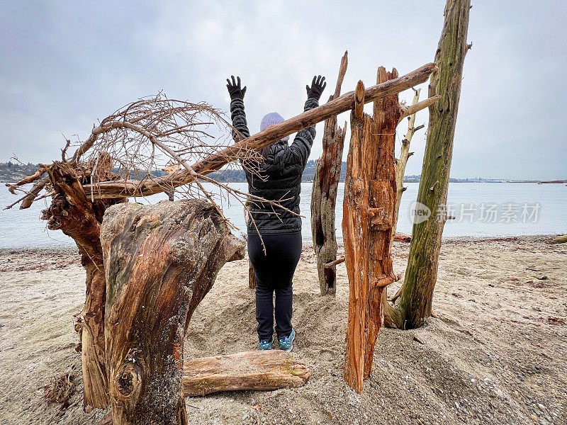 女子站在浮木堡，在海滩上举起手臂