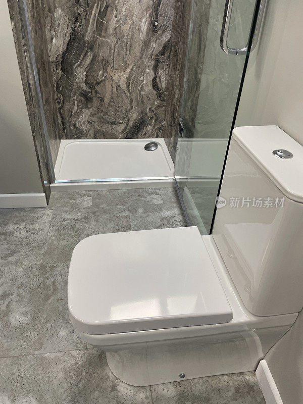 现代浴室形象，玻璃门后面有大型矩形独立淋浴间，方形白色淋浴盘，镀铬排水，黑色、灰色和白色大理石墙砖，白色卫生间，现代卫生间室内设计