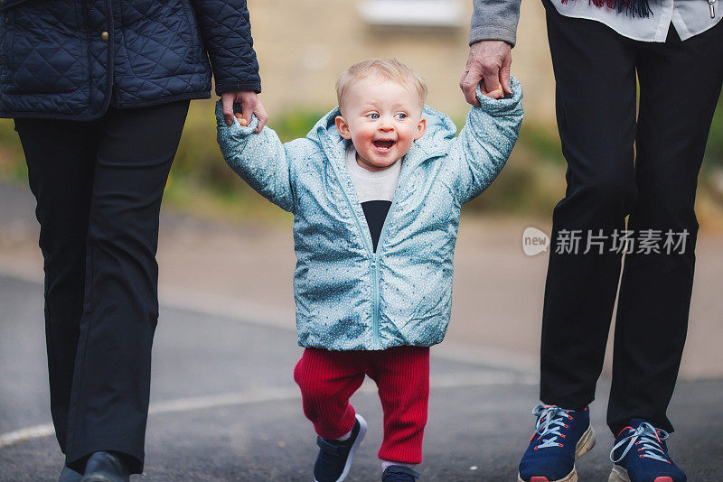 年轻的妈妈带着她快乐、兴奋的女儿在祖母的帮助下，在住宅区的人行道上走着她的第一双“新鞋”。