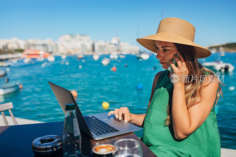 一位自由职业女性坐在海边的咖啡店里用智能手机打电话