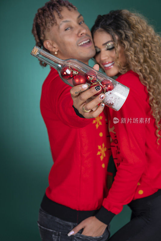 在他们的圣诞照片拍摄中，身穿红色圣诞麻袋和绿色墙背景的非洲裔拉丁夫妇相互拥抱，展示了彼此的爱意