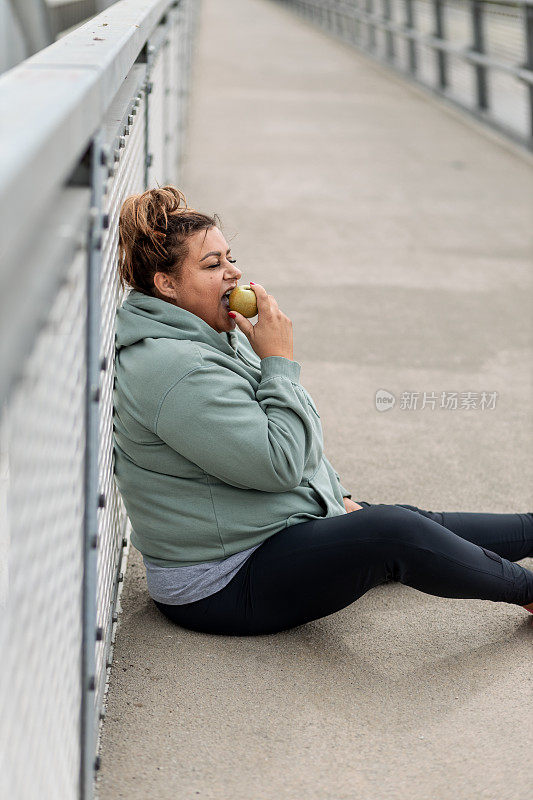 一个超重的女人在跑步后吃苹果