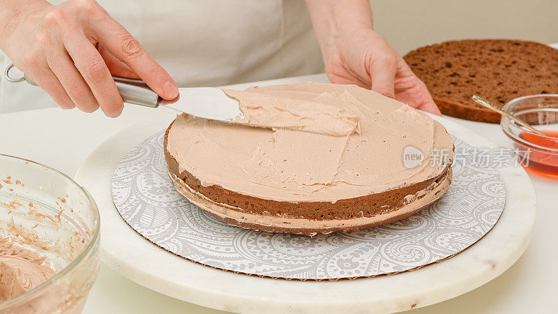 组装蛋糕。女人用手在蛋糕上涂上巧克力奶油。一步一步的巧克力蛋糕食谱