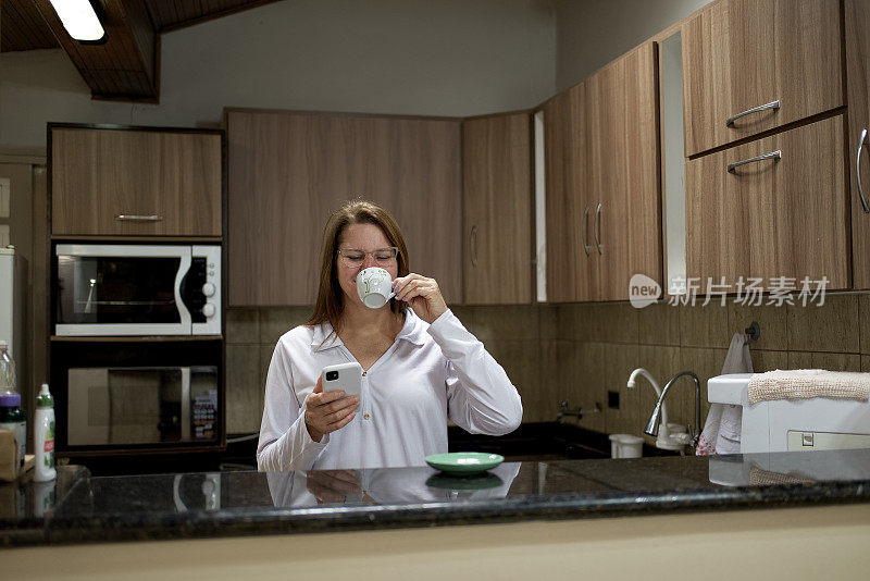 一个现代家庭里的成熟女人，用她的手机，喝着早上的咖啡
