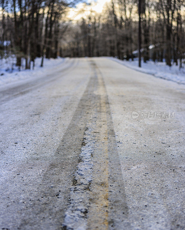 冬天，在光秃秃的树木覆盖着积雪的森林里，道路上的轮胎印。