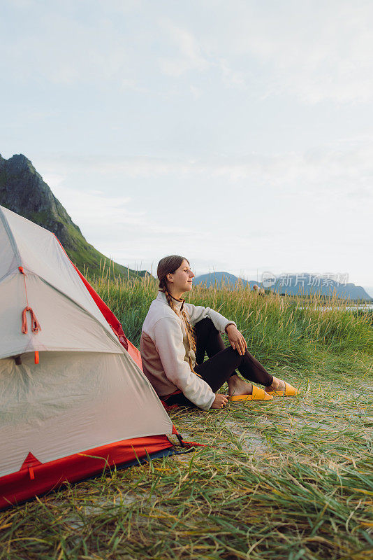 在罗浮敦群岛，坐在帐篷边的女性在海滩上凝视日落的侧面视图