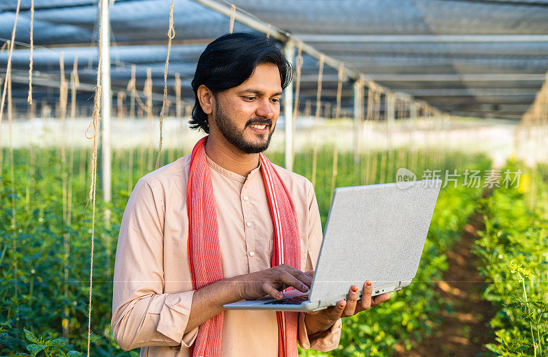 快乐的年轻农民忙于笔记本电脑在温室-现代农业的概念，技术和发展或增长。