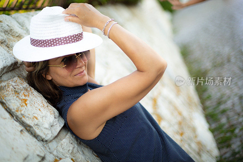 女人戴着夏天的帽子在海滩上度假，站着一张快乐的脸，微笑着自信的微笑