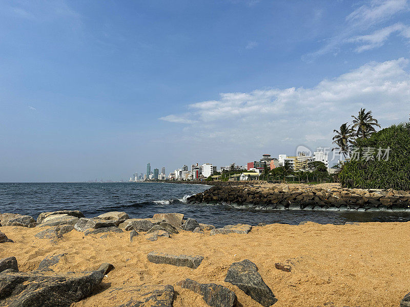 斯里兰卡科伦坡的拉维尼亚山海滩图片，沙滩和岩石海滩，大海和首都在背景中可见，海岸侵蚀防御设施和晴天的蓝天