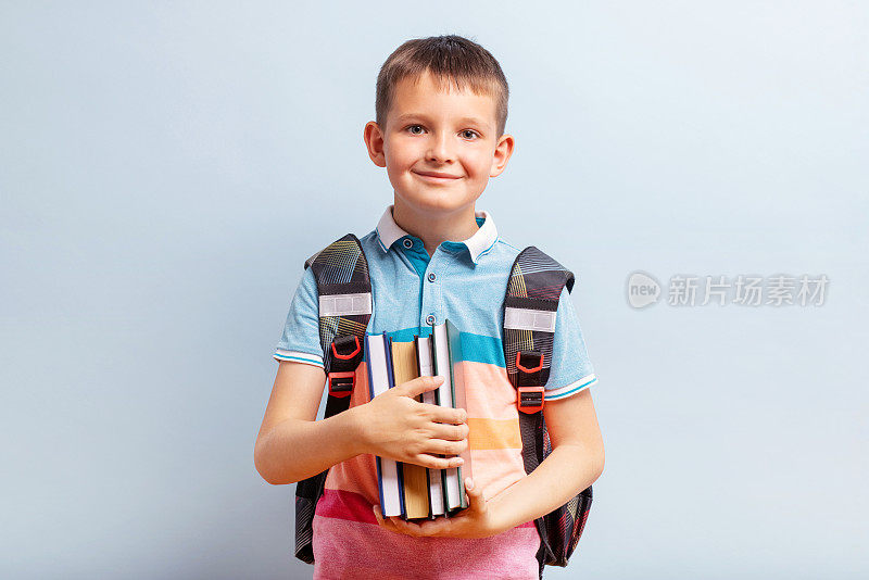 学校男孩背着书包，拿着蓝色背景的教育概念书