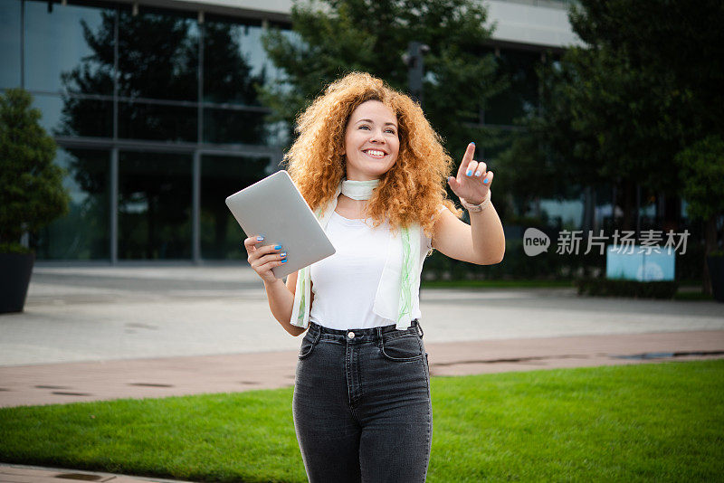 一个美丽的红发年轻女子在街上使用平板电脑的肖像