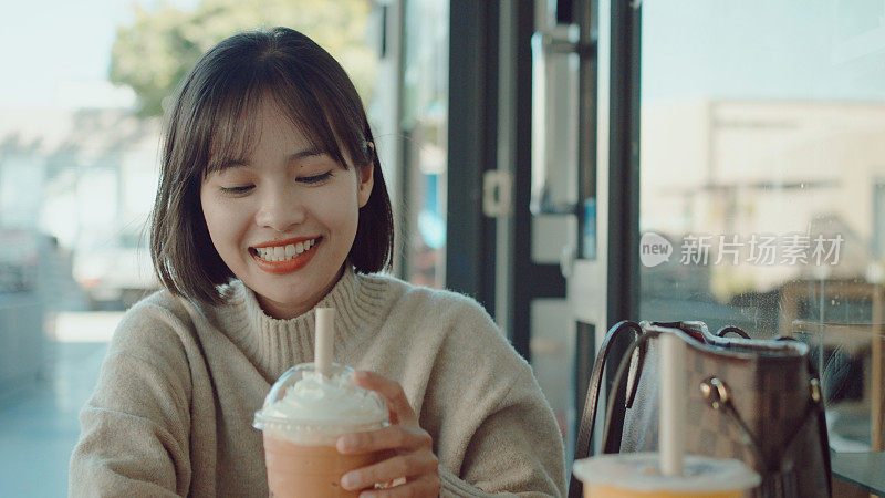 欢快的亚洲年轻女子和朋友在咖啡馆享受她的泰国奶茶冰沙冷饮