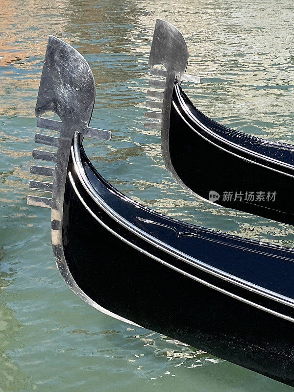 意大利威尼斯，威尼斯泻湖滨水区，漂浮在运河水面上的贡多拉(船头铁)的特写图像，聚焦于前景
