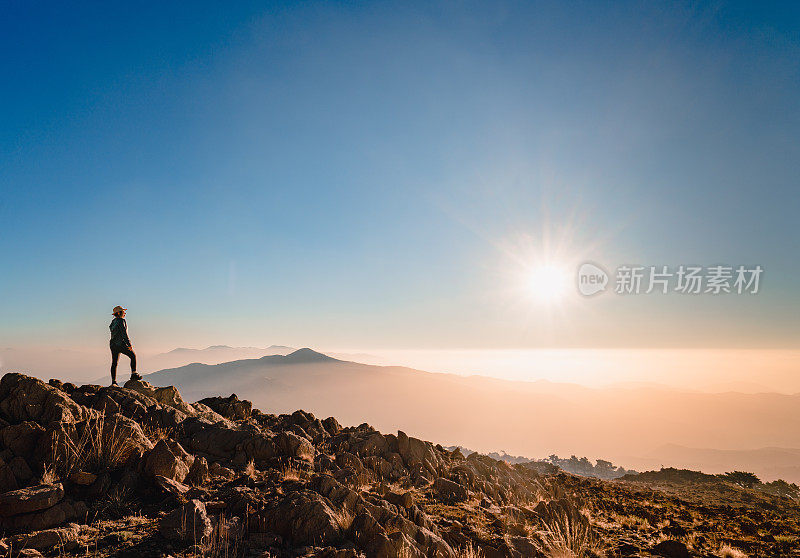 一个登山妇女的剪影在山顶上看日出