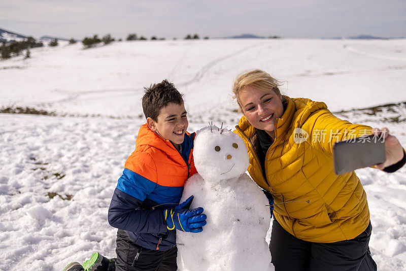 白人母亲和儿子和他们刚堆的雪人自拍