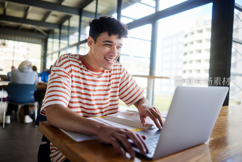 年轻的男大学生在自助餐厅用笔记本电脑工作时大笑