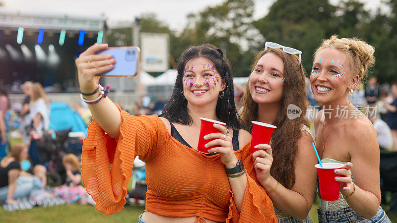 三位女性朋友在夏季音乐节上拿着饮料，戴着亮片自拍