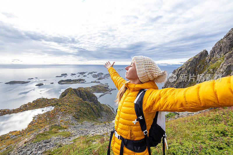 一名女子在挪威的山区徒步旅行，她张开双臂拥抱大自然