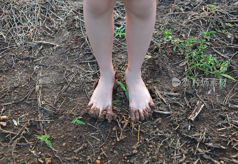 孩子光着脚走在乡下的路上，脚上满是泥。