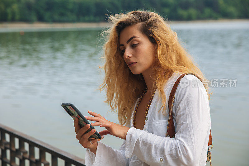 河边的卷发女人若有所思地看着电话