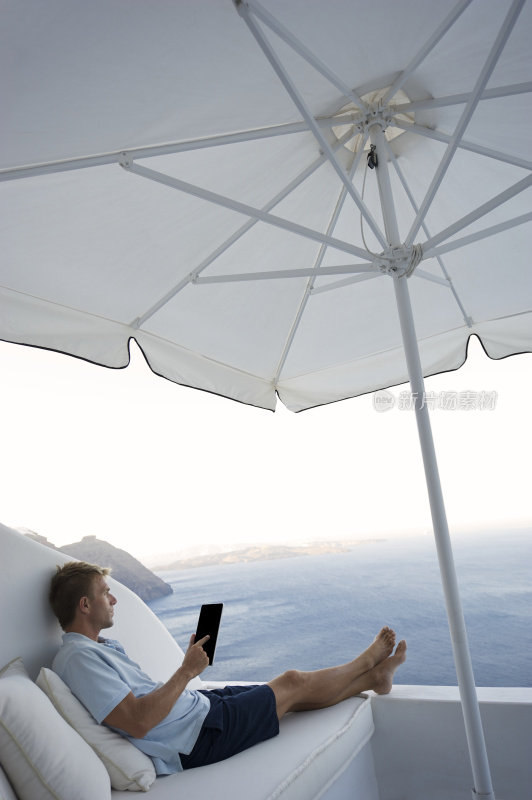 休闲男人在明亮的海边阳台上用平板电脑