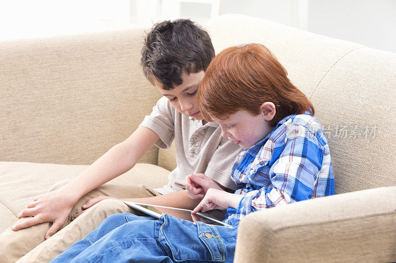 两个男孩坐在沙发上用电子平板电脑在家