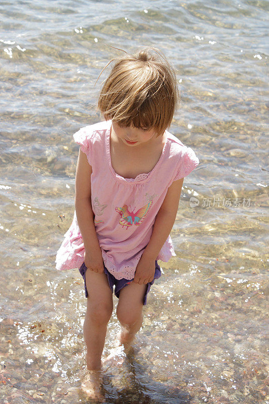 小女孩提着裤子小心翼翼地走过湖水