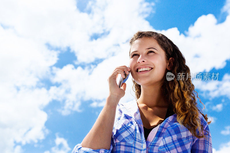 微笑年轻的美丽聊天智能手机在乌云下的天空