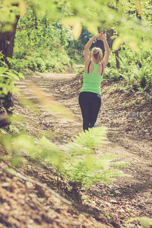 年轻的金发女人在森林里奔跑，伸展身体