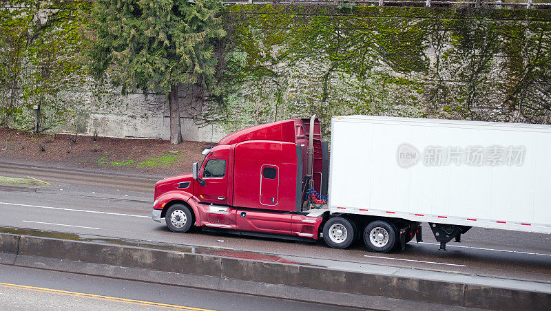 红色半卡车和拖车在高速公路上行驶，四周是爬满常春藤的石墙