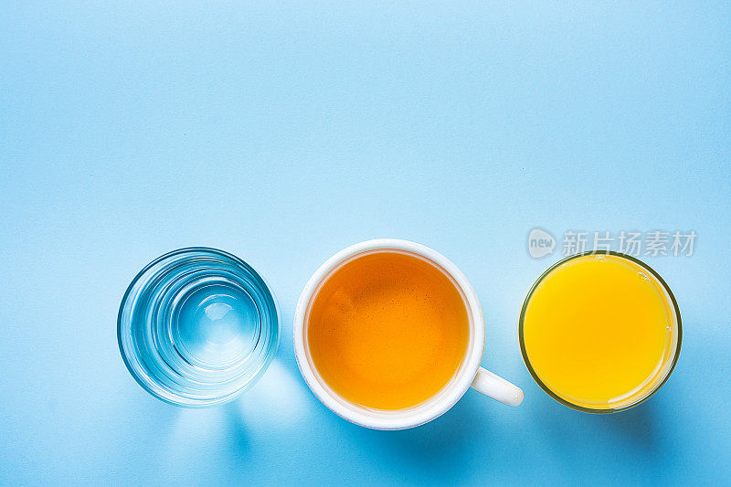 一杯新鲜压橙，柑橘汁，草本茶水在浅蓝色的背景。健康的早餐饮料。新鲜排毒。时髦潮人现代风格复制空间