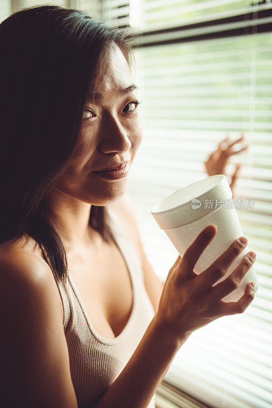 一个中国女人拿着杯子对着窗户