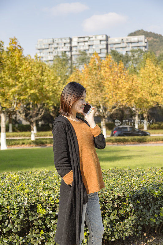 年轻的亚洲孕妇在公园里打电话