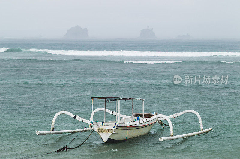 一艘白色传统巴厘岛渔船在暴风雨和大雨中波涛汹涌。Candidasa海滩