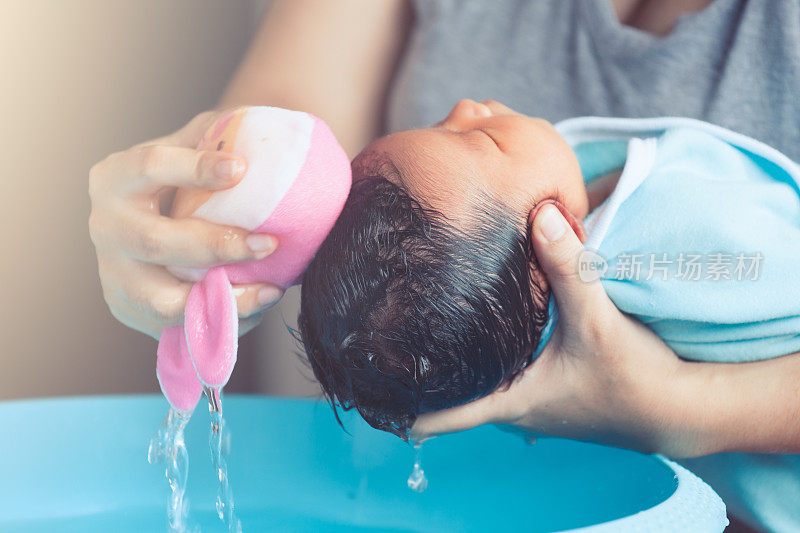 可爱的亚洲新生女婴在洗澡。妈妈用海绵清洁婴儿的头发