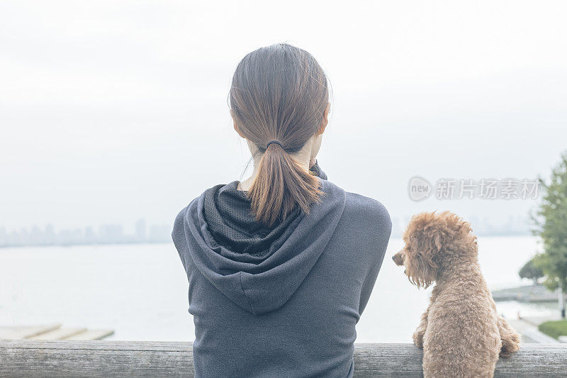 后视图的女人和可爱的小狗靠在栏杆上看风景