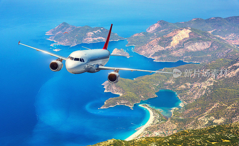 在晴朗的日子里，飞机在美丽的岛屿和地中海上空飞行。白色的客机，山脉和蓝色的水。客机。商务旅行。商用飞机
